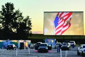 Movie getting ready to start at dusk. The American flag waving on the drive in screen before the feature movie begins