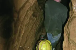 A tight squeeze as two young men squeeze through a tight passage wearing a blue and yellow helmet at Bluespring Caverns