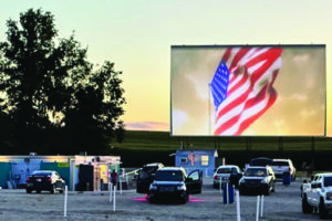 Movie getting ready to start at dusk. The American flag waving on the drive in screen before the feature movie begins